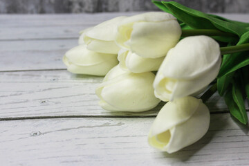 Spring white tulip bouquet on the white wooden background. Holiday greeting card concept. Copyspace for text.