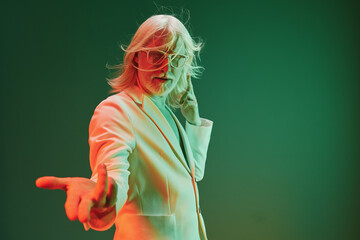 Stylish elderly man with long hair in a trendy suit posing dynamically against a vibrant green...