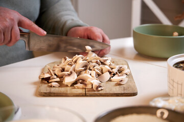 man cuts mushrooms on a wooden board on the kitchen table , close-up