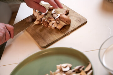 man cuts mushrooms on a wooden board on the kitchen table , close-up