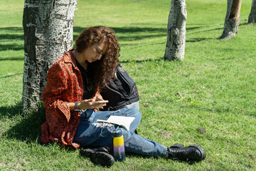 Young student using smartphone under tree in park during sunny day