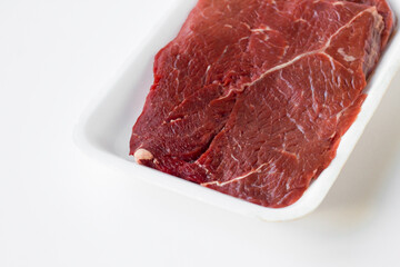 Uncooked beef fillet, on a foam plate on a white surface with copy space