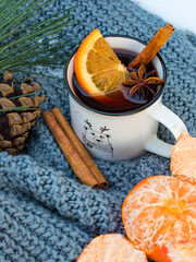 A cup of mulled wine, a cinnamon stick, an anise star on a knitted blanket, on the snow in the forest.