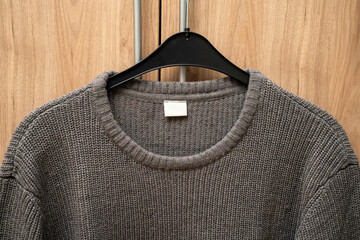 Sweater hangs on a coat hanger, that is hanging at the handle of a wooden closet.