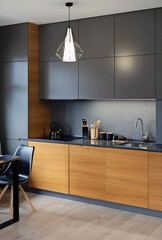 Modern kitchen interior with kitchen furniture in dark colour, wooden cabinet and kitchen sink with tap. Home design in new apartment with dining table and chair. Vertical.
