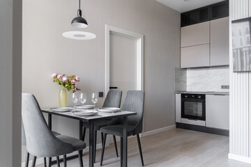 design of modern apartment in calm shades of gray and beige. Kitchen interior. plates, glasses, and vase of pink flowers on kitchen table. table and grey chairs in kitchen. Modern flat. inside home