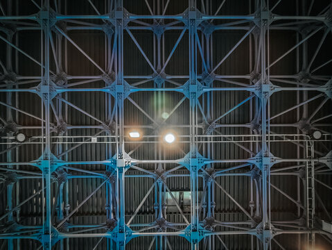 A detailed view of an industrial metal ceiling with an intricate grid structure. The blue lighting highlights the strong framework, showcasing engineering and architectural design in a modern facility