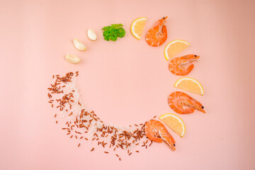 Creative food composition with boiled shrimp, lemon slices, garlic, parsley and a mixture of red and white rice on a pastel pink background.