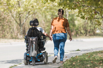 Man in a wheelchair holding hands with his girlfriend in a leisure walk. Support, love...