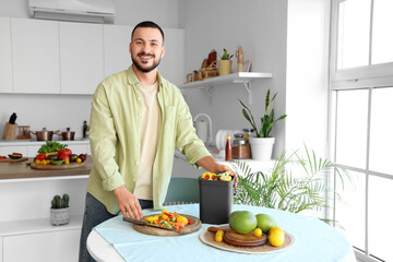 Young man with compost bin and vegetable scraps during cooking in kitchen
