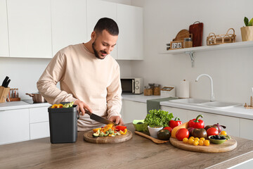 Young man with compost bin and vegetable scraps during cooking in kitchen