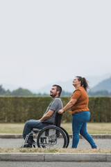 Naklejka premium Happy and smiling man with physical disability and his female assistant having a great time together while walking outdoors.