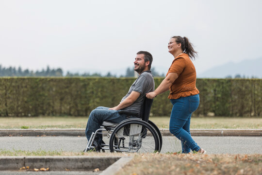 Happy and smiling man with physical disability and his female assistant having a great time together while walking outdoors.