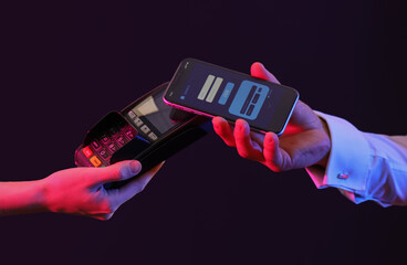 Man with mobile phone paying via terminal on dark background