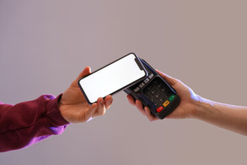 Man with blank mobile phone paying via terminal on grey background