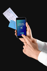 Man with mobile phone and credit card booking tickets online on black background