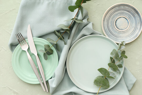 Stylish table setting with plates, cutlery and eucalyptus branches on green grunge background