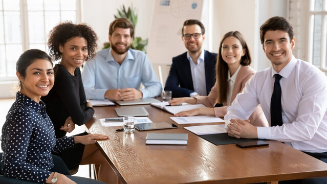 Small group of businesspeople posing for camera gathered together at conference table to solve work-related matters, planning cooperation, decision-making, joint project discussion. Unity, teamwork