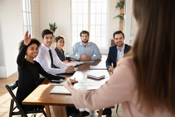Multi-ethnic professionals take part in business meeting or training, African female seminar participant raising her hand, active participating in briefing, ask question or voting, takes initiative