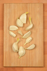A top-down shot of peeled garlic cloves arranged on a light wooden cutting board, ready for cooking