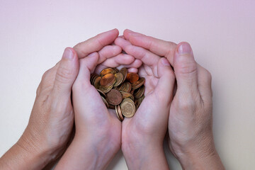 Child's hands with coins held by the hands of an adult, symbol of future savings.