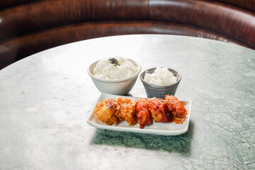 Crispy and Spicy Korean fried chickenon white plate with pickled radish,rice on marble table,Traditional Korean food,Korean foods served on a dining table,The street food of Korea.