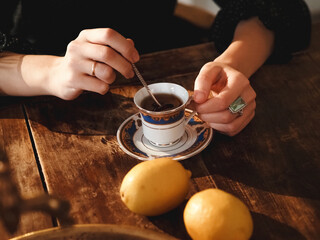Beautiful female hands holding a cup and spoon in a vintage interior. Tea with lemon