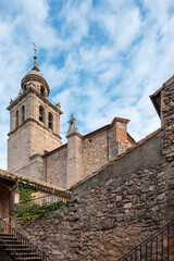 Fototapeta premium Historic stone church tower rises above picturesque village streets under bright, cloudy sky, Roman ancient town Medinaceli, Spain