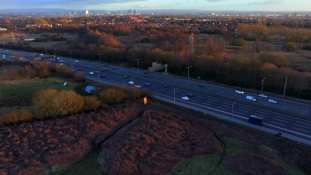 Aerial video of M60 outer ring road traffic near Swinton and Manchester city skyline at Sunset. 