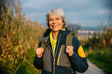 Senior hiker woman smiling and hiking in nature during golden hour