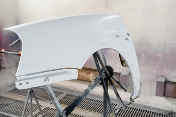 A primed car fender set up for painting in an auto body shop. The panel is mounted on a stand...