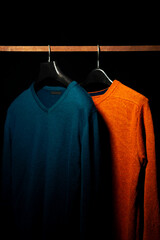 Obraz premium Plain Orange And Teal Sweatshirts on Hanger, Isolated on Black Background