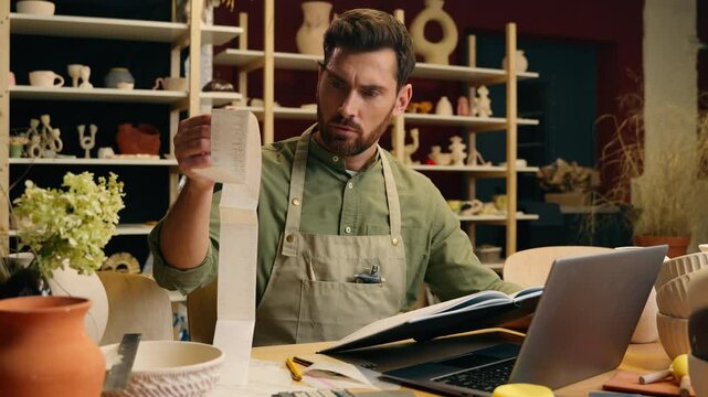 Shocked frustrated Caucasian man male small business owner potter gut businessman examining large bill check receipt debt bankruptcy shock payment problem unpaid tax accounting laptop in pottery store