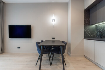 Multifunctionality of the studio apartment space. There is a living area with a TV and a dining area with a dining table and a kitchen.