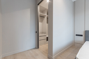 A bedroom in the apartment with a bed and an entrance to a dressing room equipped with cabinets and shelves.
