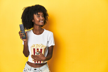 African-American teenage girl with popcorn, enjoying cinema concepts on yellow backdrop.