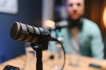 Focus on professional microphone and podcast host in background