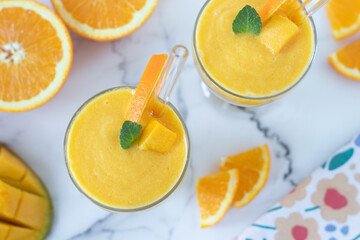 Mango orange smoothie on white marble kitchen table with fresh fruit. Top view. Homemade cold blended drink for breakfast.