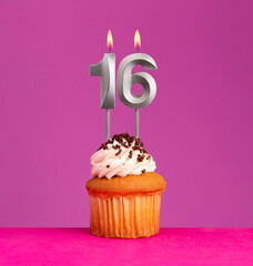 Birthday candle number 16 with cupcake on violet background.