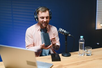 A video blogger records content in his studio. The host of the video blog is a young man who is...