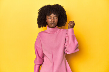 Teen girl in pink sweatshirt, yellow studio backdrop showing fist to camera, aggressive facial...