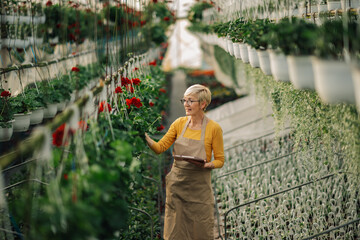 Old female florist with clipboard at hothouse checking on vertical garden