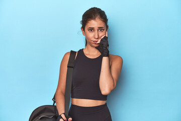 Sporty teen with gym bag, ready for a workout biting fingernails, nervous and very anxious.