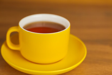 A mug with a yellow saucer stands on a wooden table, fragrant black tea is poured into it. High quality photo