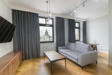A small cozy living room with a magnificent view of the city from the window. Parquet floor, stylish upholstered furniture.