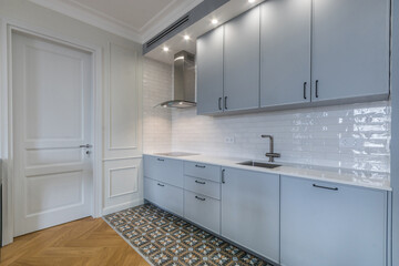 Laconic kitchen design with white walls and multicolored floor tiles. Blue kitchen set with built-in appliances.