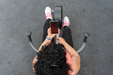 Woman using smartphone while exercising outdoors on a stationary bike