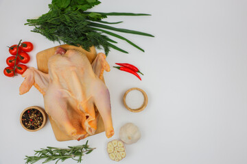 A raw processed chicken carcass lies on a wooden board with spices in wooden bowls, herbs, herbs...