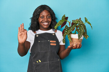 Curvy gardener holding plant in studio cheerful and confident showing ok gesture.
