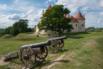 Two old vintage retro cannon guns. Latvian tourist landmark attraction - medieval Bauska castle on background. Bauska, Latvia.